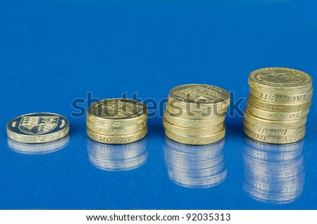 Ascending stacks of coins isolated on blue background with reflection / Rising stack of pound coins
