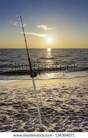 Fishing pole against ocean at sunset
