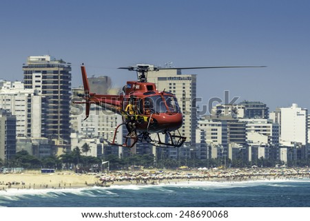 RIO DE JANEIRO, BRAZIL - JANUARY 2015:Rescue helicopter with lifeguard bombeiros flying over crowded Copacabana Beach during hot summer day in Rio de Janeiro, Brazil.