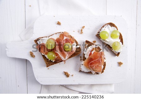 Snack of whole grain bread with soft cheese and ham and sweet grape