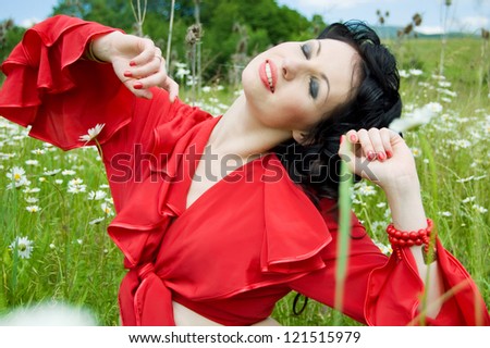 alluring gypsy woman sitting and stretching herself in a green field of daisies. attractive woman dressed like a gypsy with closed eyes on the background of a green field