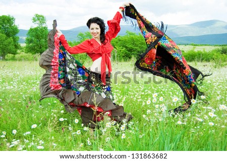 illustration of a beautiful gypsy woman dancing with colorful shawl in a green field of daisies. attractive dark-haired woman dressed like a gypsy waving her skirt and shawl and smiling