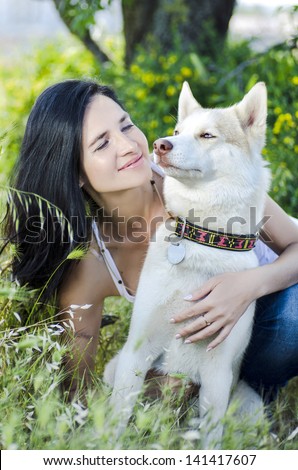 Alluring young woman and white husky outdoors.Happy brunette woman looking at siberian husky dog, sitting in green forest in shadow and smiling, on a walk with dog