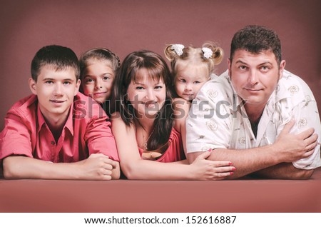 Happy family smiling, posing, having fun in studio. beautiful father, mother, son and two daughters playing in studio on brown background. loving family with three children