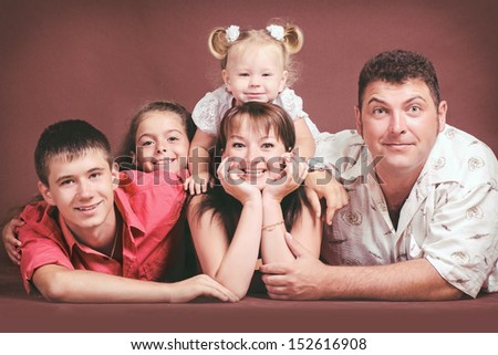 Happy family smiling, posing, having fun in studio. beautiful father, mother, son and two daughters playing in studio on brown background. loving family with three children