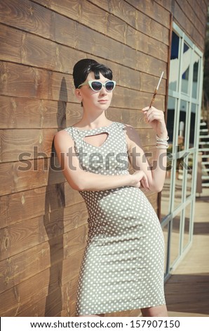 beautiful brunette woman relaxing in luxury hotel restaurant. Stylish rich slim girl in retro dress at villa apartment. glamorous lady in sunglasses, with cigarette holder.vacation. Retro style