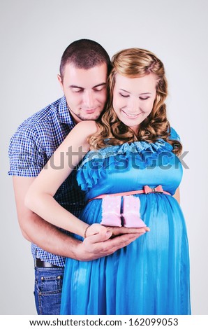 Beautiful young pregnant couple posing in studio. happy and healthy pregnancy. happy smiling couple in casual trendy wear showing baby shoes ugi. isolated on white