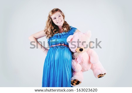 Beautiful pregnant woman in studio. Blonde pregnant woman with teddy bear on white background. Happy pregnancy. Romantic pregnant girl smiling. Attractive pregnant woman in stylish blue dress.