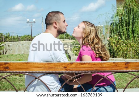 lovely young couple sitting on seat bench with view to summer park. Happy romantic couple on a date outdoors.