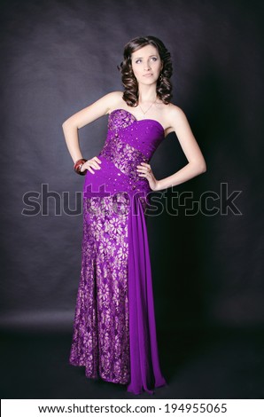 Beautiful fashionable woman in studio. Fashion portrait of young sexy alluring woman girl in elegant evening lilac dress posing on black background