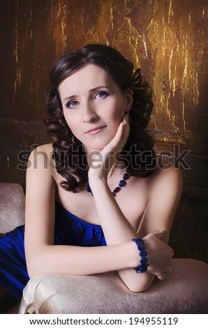 Beautiful fashionable woman indoors. Fashion portrait of young sexy alluring woman girl with perfect skin healthy curly hair natural makeup in blue dress