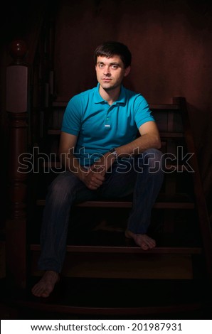 Handsome man wearing summer casual clothes sitting on stairs indoors. young brutal man posing in studio. sexy stylish guy model. male fashion