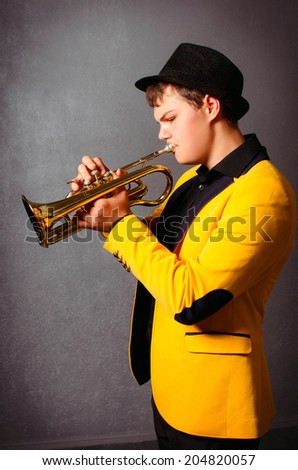 Handsome blind trumpet player in hat and yellow jacket playing trumpet. Portrait of young musician playing the trumpet at studio.