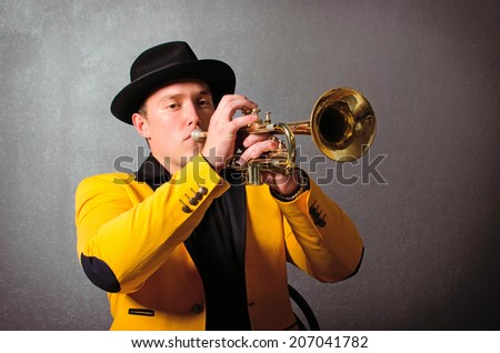Handsome jazz trumpet player in hat and yellow jacket playing trumpet. Portrait of young musician playing the trumpet at studio.