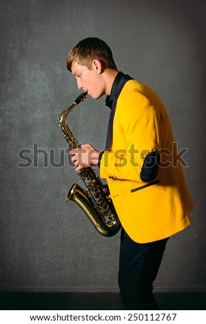 Handsome musician saxophonist playing saxophone. Young saxophone player in studio. Jazz-band