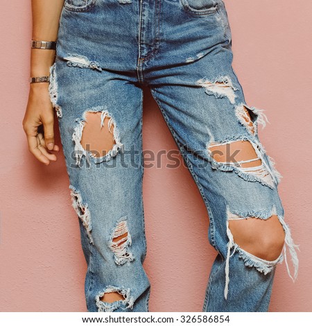 Lady in fashionable ripped Jeans stands in pink wall