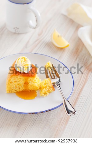 Slice of lemon polenta cake with lemon syrup and whipped cream on a plate, selective focus