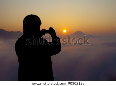 Young man with compact camera, standing on cliff\'s edge and taking a photo