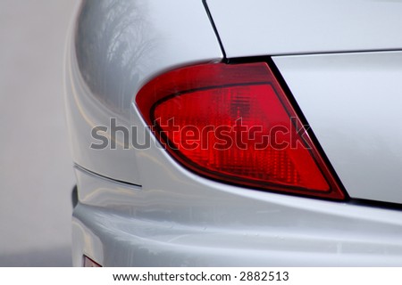 Detail of the rear end of a silver car with focus on the brake lights.