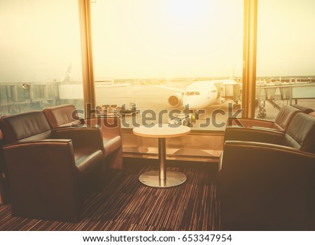 Departure lounge at the airport with seating and table with aircraft preparing for flight in the background