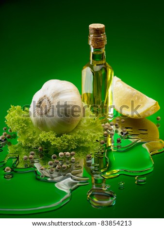 bottle with oil standing on a mirrored  background surrounded by garlic, lettuce, lemon, pepper and drops of oil