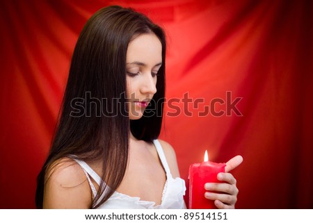 Young woman with candle in studio against red background