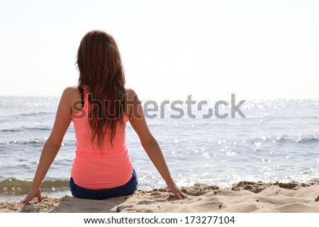 Beach holidays woman back view enjoying summer sun sitting in sand looking happy at copy space. Beautiful young model
