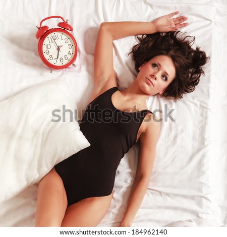 Sexy lazy girl lying with alarm clock on the bed. Young woman relaxing lazing in her bedroom at the morning.