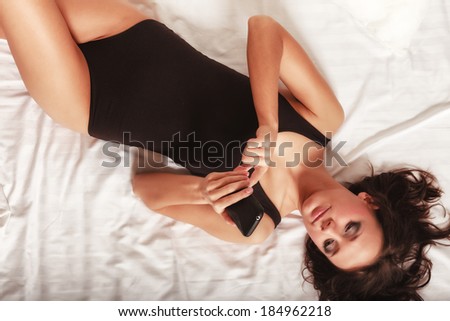 Sexy lazy girl lying on the bed texting on mobile phone. Young woman relaxing lazing in her bedroom at the morning.