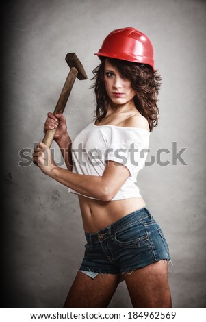 Sex equality and feminism. Sexy girl in safety helmet holding hammer tool on gray. Young attractive woman working as construction worker. Studio shot.