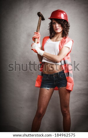 Sex equality and feminism. Sexy girl in workwear safety helmet and orange vest holding hammer tool on gray. Young attractive woman working as construction worker. Studio shot.