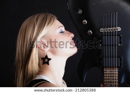 Rock music. Blonde girl guitarist musician performer with electric guitar musical string instrument on black. Concert.
