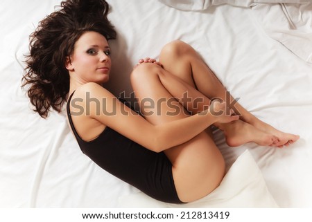Sad unhappy girl in black body lying in fetal position on bed. Young lonely woman relaxing lazing in bedroom. Depression.