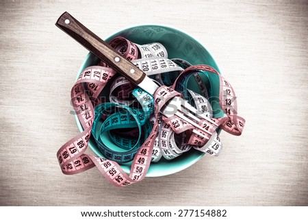 Diet food healthy lifestyle and slim body concept. Many measuring tapes in bowl on table with fork, top view