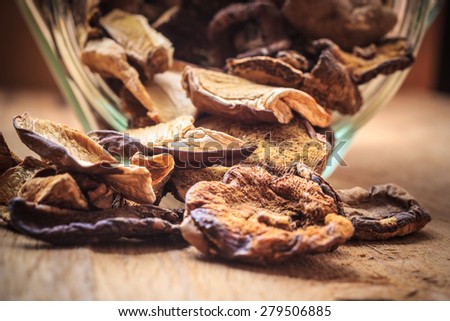 Food. Closeup dry mushrooms spilling out from storage jar on wooden surface table background.