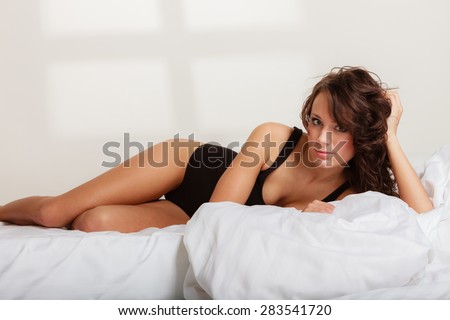 Sexy lazy girl in black body underwear lying on the bed. Young woman relaxing lazing in her bedroom at the morning.