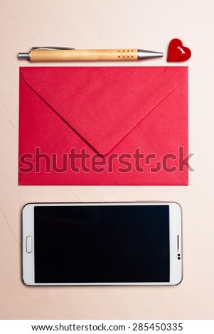 Red envelope little heart, pen and smart phone on wooden surface.