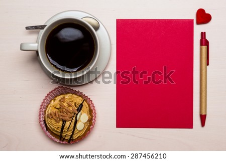 Coffee cup sweet cake cupcake and red paper blank with pen on wooden surface, top view copy space for text
