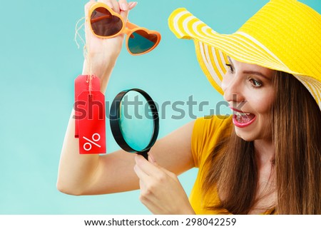 Good shopping summer sale concept. Fashionable woman choosing sunglasses searching through magnifying glass, discount red label with percent sign in hand
