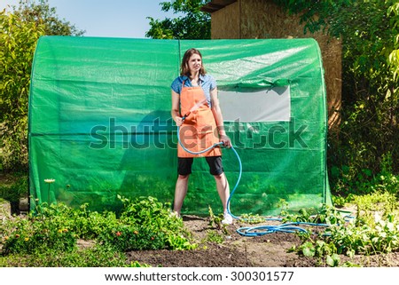 Gardening. Woman in orange apron holds the sprinkler hose for irrigation plants watering the garden outdoor