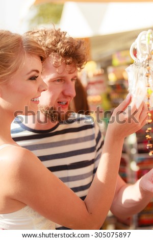 Summer holidays shopping concept. Young couple of tourists buying souvenirs in gift street stall outdoor