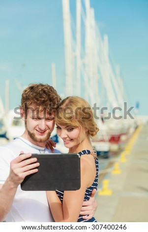 Modern technology devices and tourism concept. Young couple outdoor against sea boats with tablet enjoying summer holidays