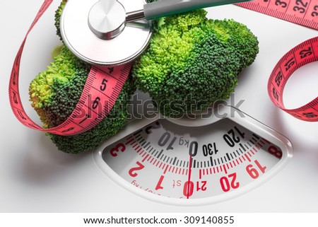 Diet healthy eating weight control concept. Closeup green broccoli with measuring tape and stethoscope on white scales