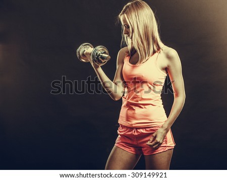 Bodybuilding. Strong fit woman exercising with dumbbells. Muscular blonde girl lifting weights studio shot on dark