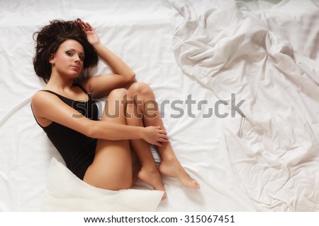 Sexy lazy girl in black body lying in fetal position on bed. Young lonely woman relaxing lazing in bedroom at morning.