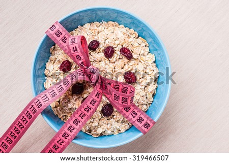 Diet healthy food weight loss concept. Oatmeal in blue bowl with measuring tape around on kitchen table