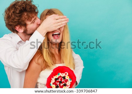 Handsome man giving woman candy bunch flowers. Young boyfriend with surprise present gift for girlfriend covering her eyes. Happy loving couple. Love.