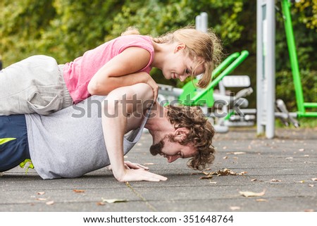 Active young man and woman exercising doing push ups. Muscular strong guy and girl in training suit working out at outdoor gym. Sport fitness and healthy lifestyle concept.