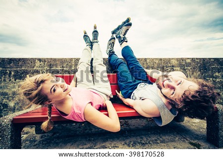 Young people friends in training suit with roller skates. Woman and man relaxing lying on bench outdoor.