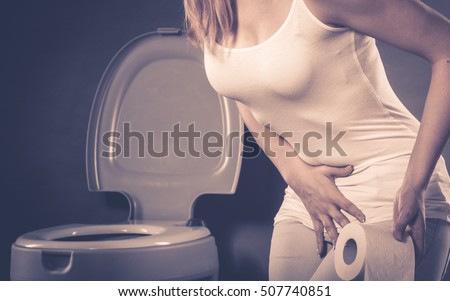 Sick woman with hands pressing her crotch lower abdomen, holding paper roll in front of toilet bowl. Medical problems, incontinence, health care concept
